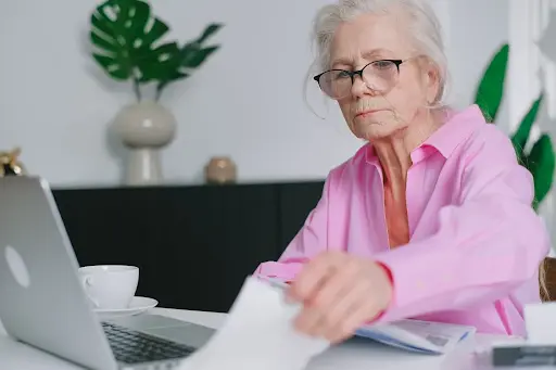 An older woman sitting at a desk using a laptop computer