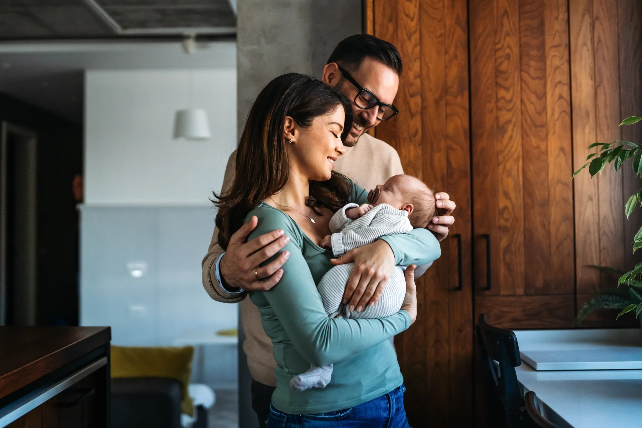 mother and father standing in a kitchen holding a newborn baby